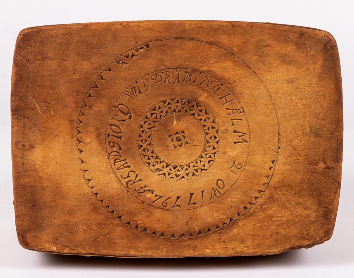 Ask med trycklock, fyrsidig, av trä, utskuret på en sida samt på locket: "LARS PDS GJORD WID DRÅNINGHÅLM 21 OW 1779". Svepteknik. På ena sidan av lådan och på dess lock är övre skiktet av svepet genombrutet av utskurna fyrarmade figurer med rött resp. vitt papper under.
