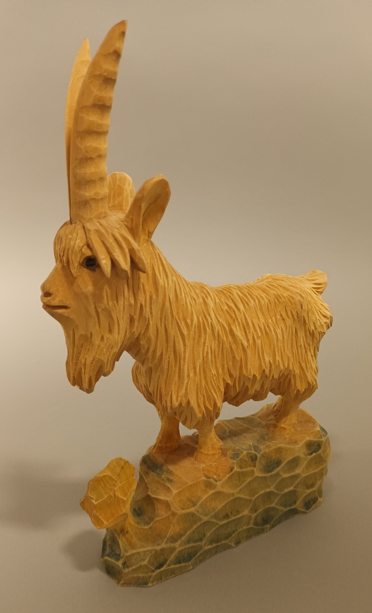 Trefigur forma som ein geitebukk. Måla på sokkeln. Merkt I.A nede på den eine sida.