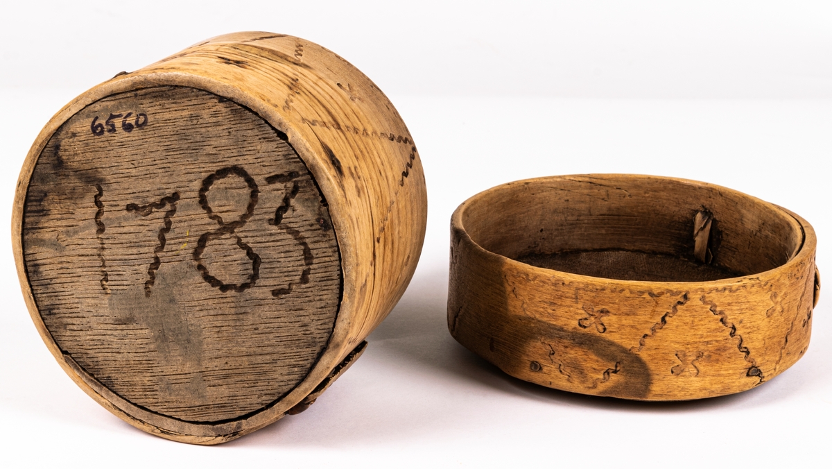 Ask, ornerad genom brännstämpling. I botten märkt 1783.
I svepteknik, rund med lock. Botten och lock av ek. Ornament: fyrbladiga rosor samt krusiga linjer.
