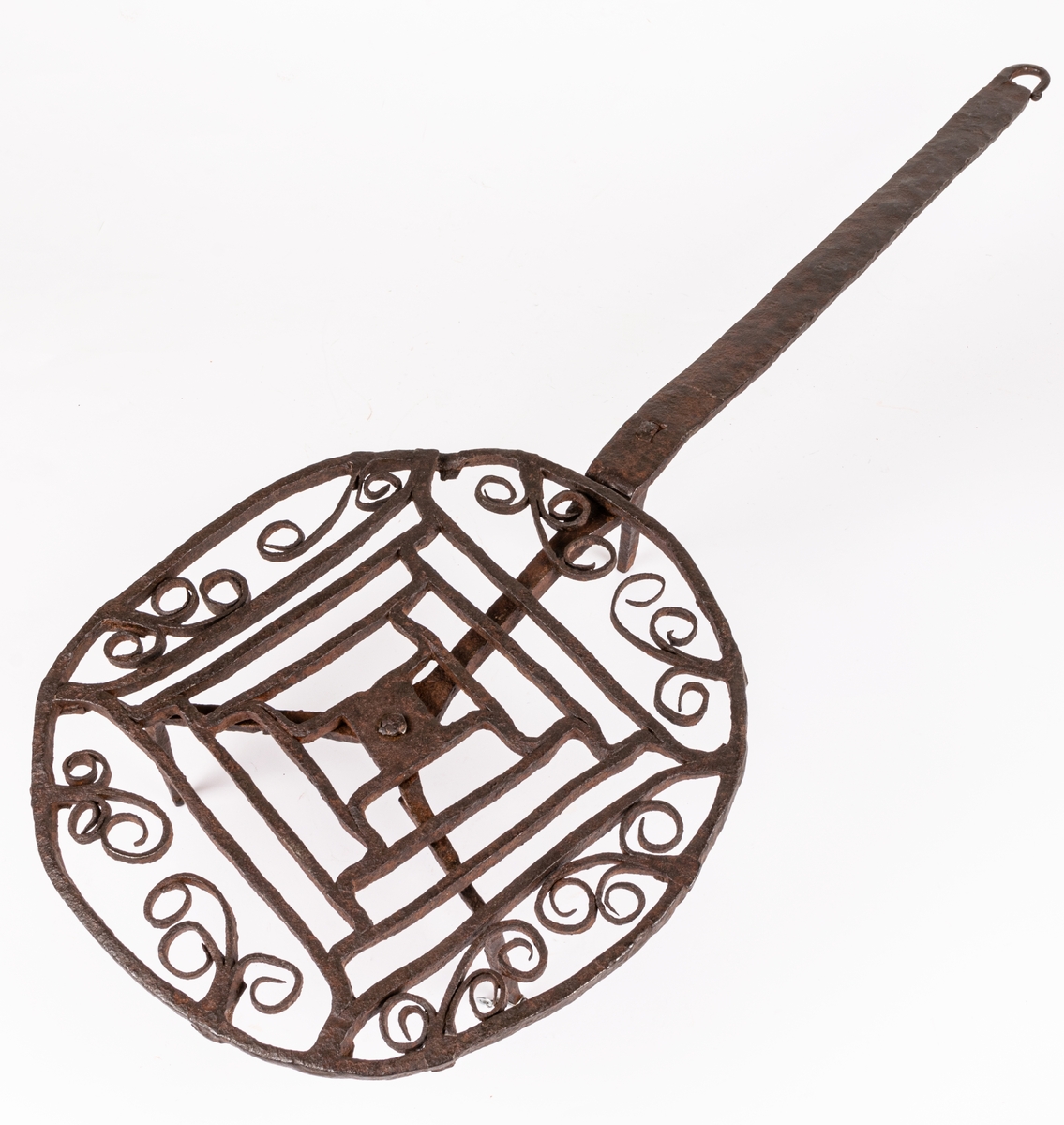 Halster av järn. Rund platta av hopsmidda tenar, jämte furkanter omgivna av cirkel och bladformiga ornament. Långt skaft, tre fötter.