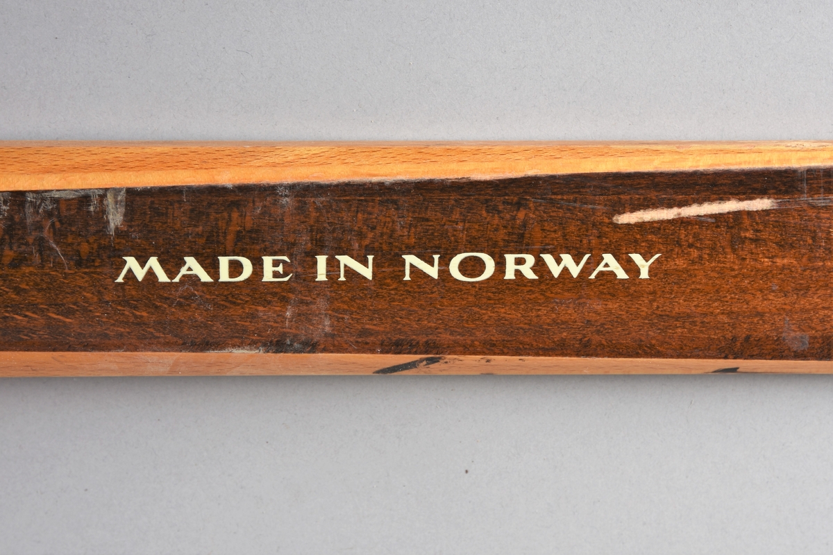 Eit par ski av tre. Kandaharbinding. Eit par skistavar. To reimer til å halde det saman. Ein reisegodslapp heng fast i B.