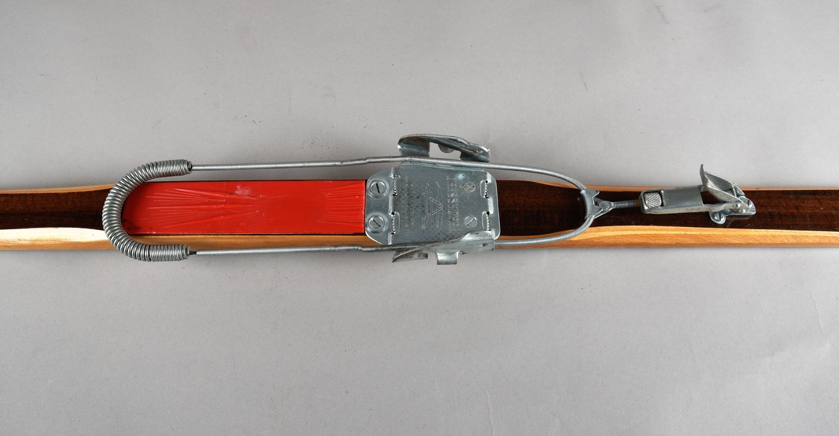 Eit par ski av tre. Kandaharbinding. Eit par skistavar. To reimer til å halde det saman. Ein reisegodslapp heng fast i B.