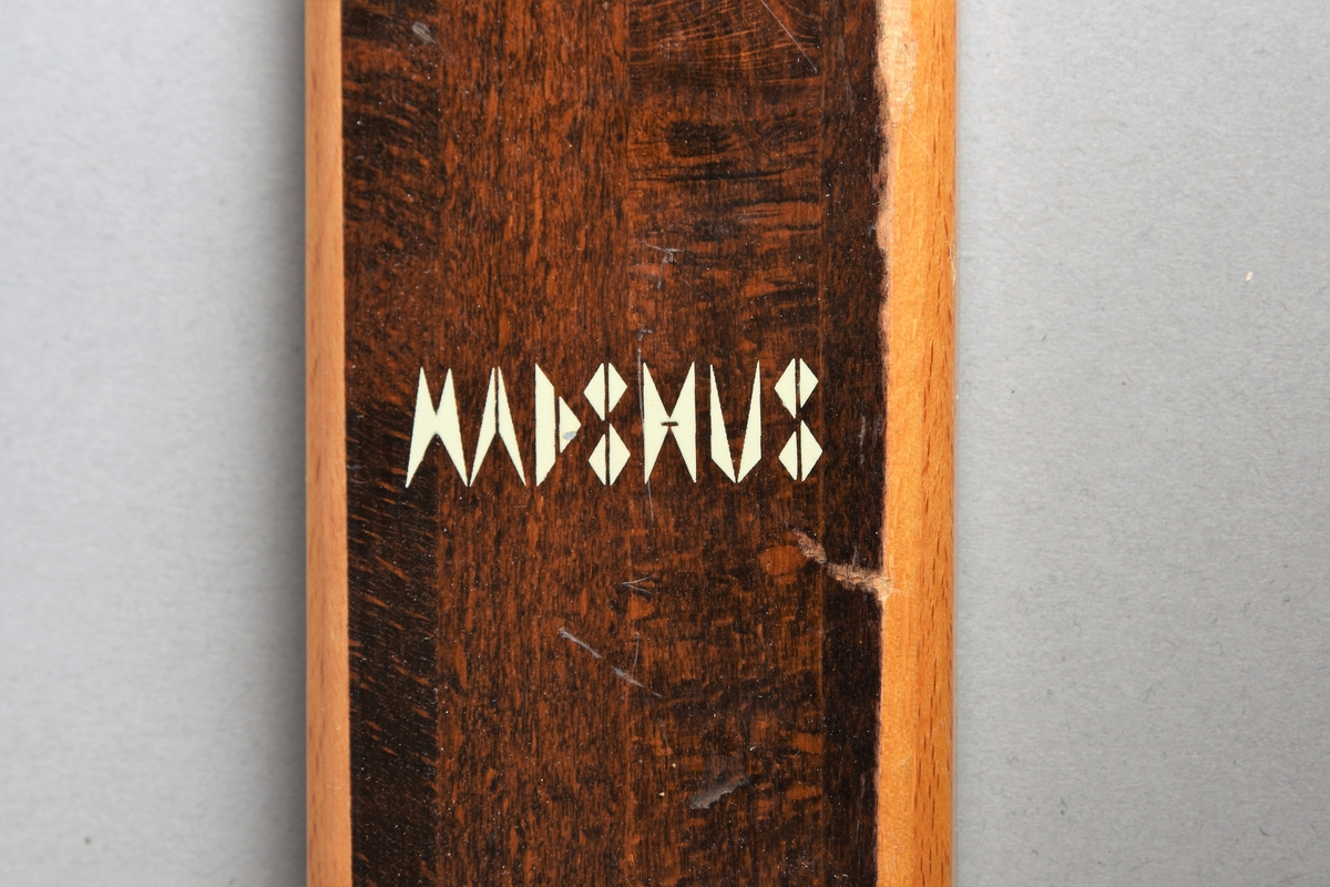 Eit par ski av tre. Kandaharbinding. Eit par skistavar. To reimer til å halde det saman. Ein reisegodslapp heng fast i B.