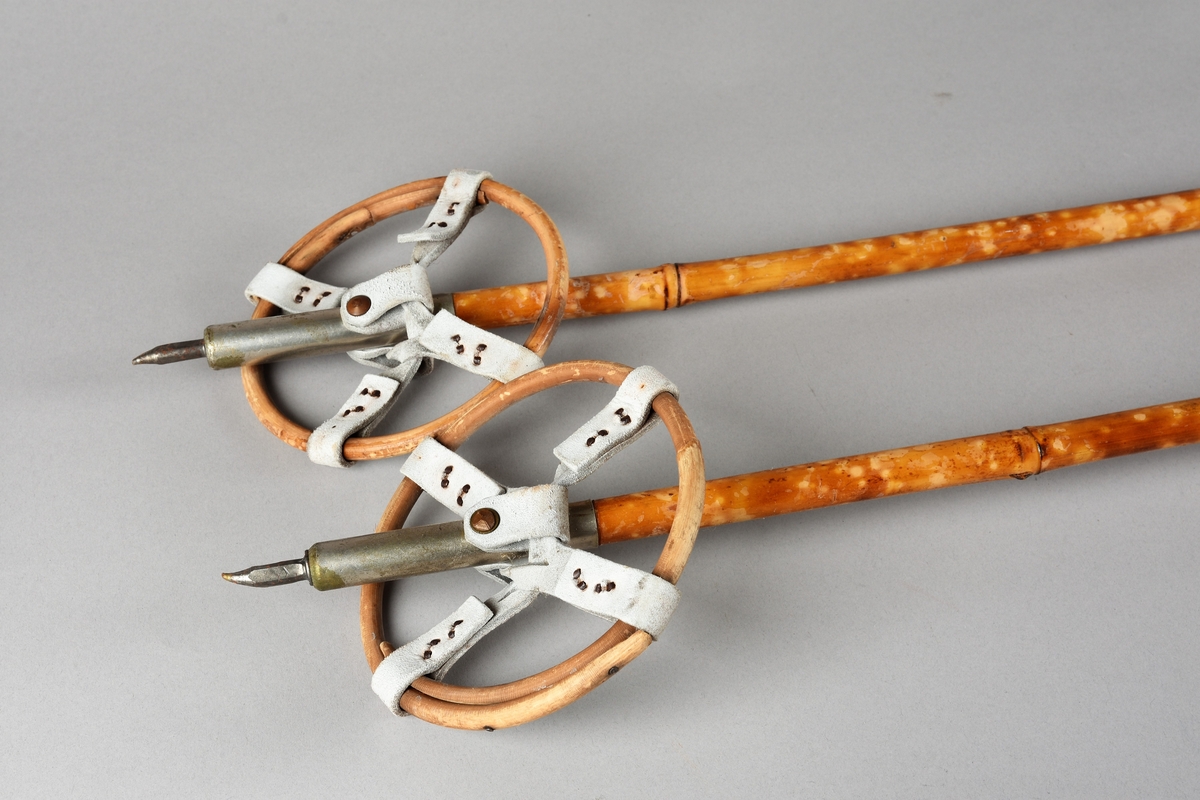 Eit par ski av tre. Kandaharbinding. Eit par skistavar. To reimer til å halde det saman. Ein reisegodslapp heng fast i B.