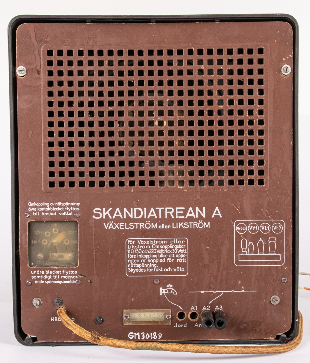 Radioapparat, med kåpa i brunsvart bakelit. Överst rektangulär högtalaröppning med tygklädsel. Nedtill horisontal stationsvisare, tre vred och två brytare. På ömse sidor om visarfönstret en örn med swastika i klorna. Text på baksidan: "SKANDIATREAN A" m.m. Nätsladd i tectil. Antell m. banankontakt. Radion är importerad av Skandia och ursprungligen en s.k. "Volksempfänger VE 301 DYN". Troligen ombygd för Sverige.