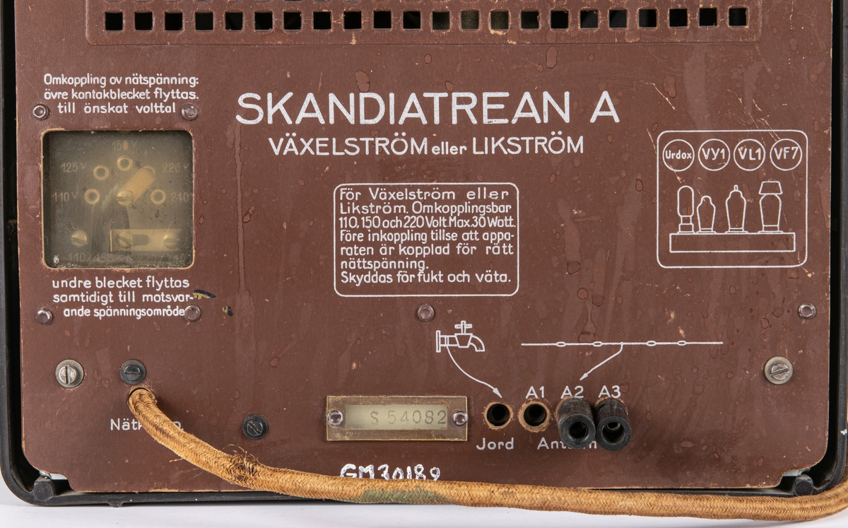 Radioapparat, med kåpa i brunsvart bakelit. Överst rektangulär högtalaröppning med tygklädsel. Nedtill horisontal stationsvisare, tre vred och två brytare. På ömse sidor om visarfönstret en örn med swastika i klorna. Text på baksidan: "SKANDIATREAN A" m.m. Nätsladd i tectil. Antell m. banankontakt. Radion är importerad av Skandia och ursprungligen en s.k. "Volksempfänger VE 301 DYN". Troligen ombygd för Sverige.