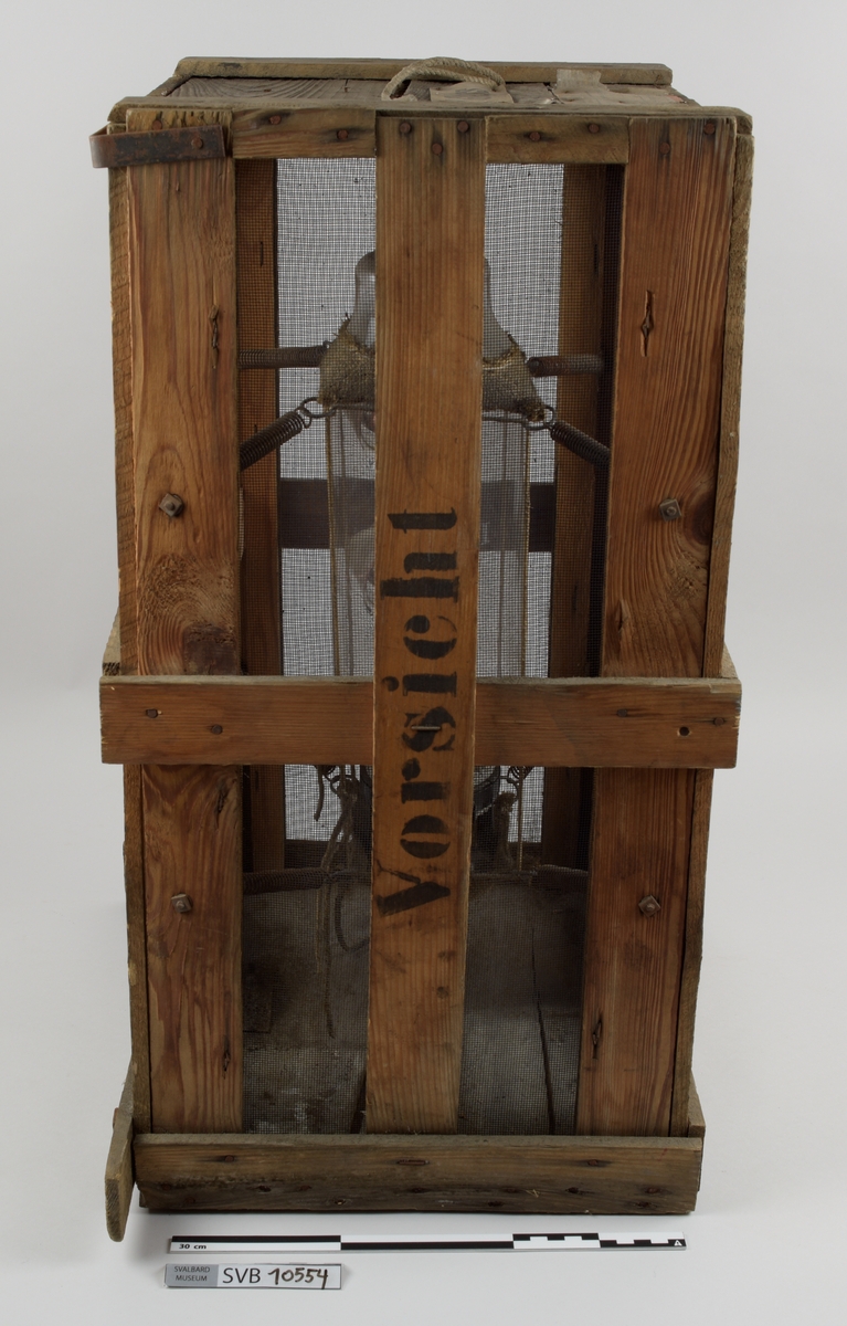 Kasse av tre. Bunnen og toppen er heldekkene, mens sidene er laget av langsgående trebord med mellomrom, avstivet med kortere bord på tvers i bunn og på midten. På innsiden av trebordene er det montert netting. Inni kassen er det montert et kortbølgeradiorør av glass og metall. Røret er suspendert i midten av kassen ved hjelp av to tekstilbiter, én i hver ende. Disse er holdt på plass av åtte metallfjærer, fire i hver ende, som er montert i kassens hjørner. Fjærene er montert ca. midt på kassens øverst halvdel og midt på kassens nederste halvdel. På den ene siden av kassens bunn er det montert to 90-graders metallbraketter. Langs toppen av den ene siden av kassen er det montert en lengre metallbrakett. I toppen av kassen er det festet tau og en papirlapp. På kassens utside er det trykket svart tekst. Trebordene holdes sammen med spiker og stifter av metall.