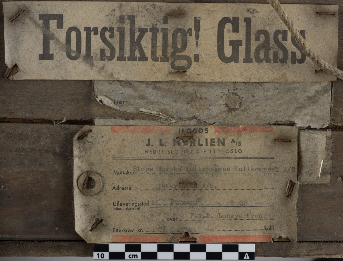 Kasse av tre. Bunnen og toppen er heldekkene, mens sidene er laget av langsgående trebord med mellomrom, avstivet med kortere bord på tvers i bunn og på midten. På innsiden av trebordene er det montert netting. Inni kassen er det montert et kortbølgeradiorør av glass og metall. Røret er suspendert i midten av kassen ved hjelp av to tekstilbiter, én i hver ende. Disse er holdt på plass av åtte metallfjærer, fire i hver ende, som er montert i kassens hjørner. Fjærene er montert ca. midt på kassens øverst halvdel og midt på kassens nederste halvdel. På den ene siden av kassens bunn er det montert to 90-graders metallbraketter. Langs toppen av den ene siden av kassen er det montert en lengre metallbrakett. I toppen av kassen er det festet tau og en papirlapp. På kassens utside er det trykket svart tekst. Trebordene holdes sammen med spiker og stifter av metall.