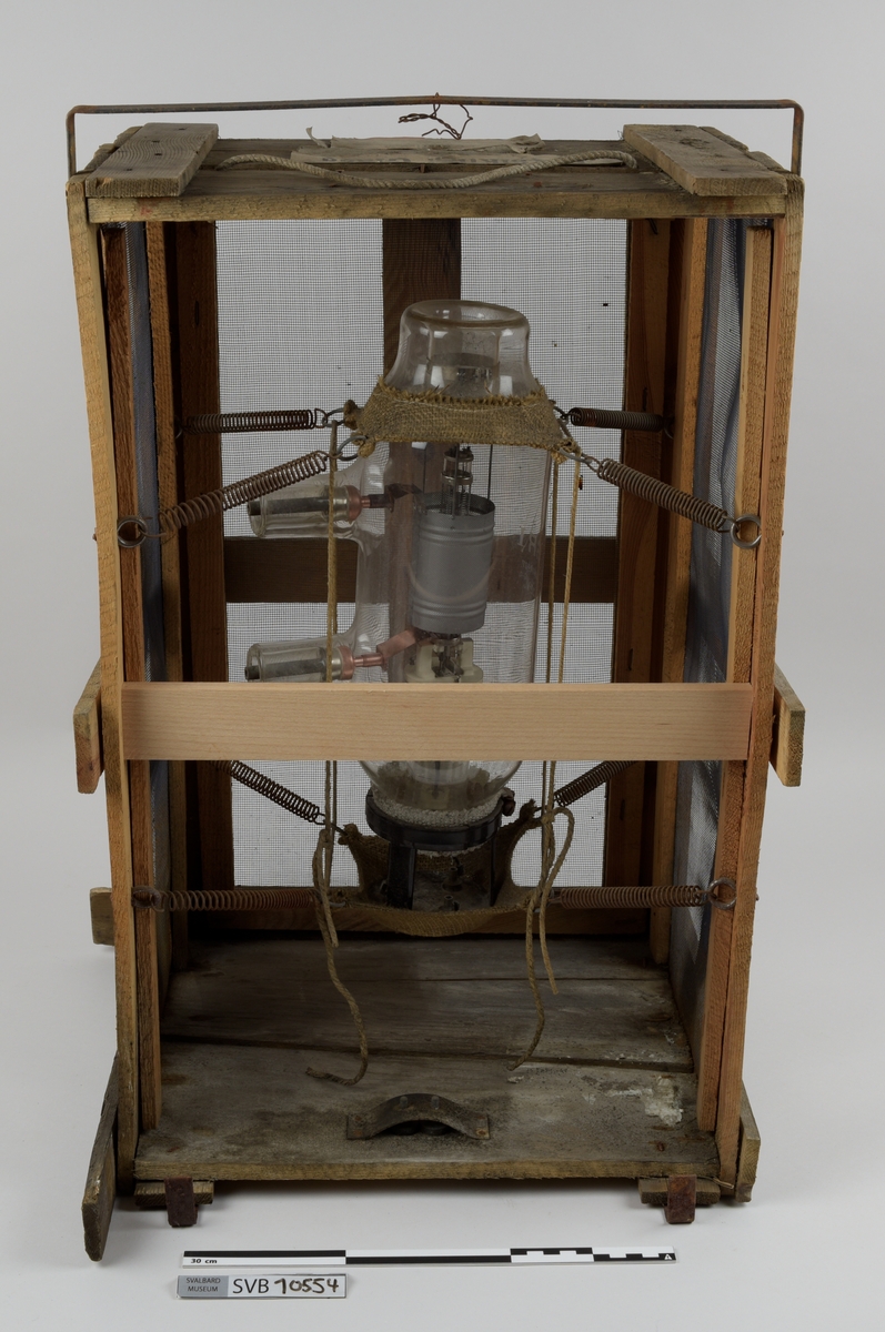 Kasse av tre. Bunnen og toppen er heldekkene, mens sidene er laget av langsgående trebord med mellomrom, avstivet med kortere bord på tvers i bunn og på midten. På innsiden av trebordene er det montert netting. Inni kassen er det montert et kortbølgeradiorør av glass og metall. Røret er suspendert i midten av kassen ved hjelp av to tekstilbiter, én i hver ende. Disse er holdt på plass av åtte metallfjærer, fire i hver ende, som er montert i kassens hjørner. Fjærene er montert ca. midt på kassens øverst halvdel og midt på kassens nederste halvdel. På den ene siden av kassens bunn er det montert to 90-graders metallbraketter. Langs toppen av den ene siden av kassen er det montert en lengre metallbrakett. I toppen av kassen er det festet tau og en papirlapp. På kassens utside er det trykket svart tekst. Trebordene holdes sammen med spiker og stifter av metall.