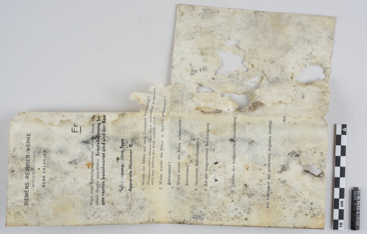 Kasse av tre. Bunnen og toppen er heldekkene, mens sidene er laget av langsgående trebord med mellomrom, avstivet med kortere bord på tvers i bunn og på midten. På innsiden av trebordene er det montert netting. Inni kassen er det montert et kortbølgeradiorør av glass og metall. Røret er suspendert i midten av kassen ved hjelp av to tekstilbiter, én i hver ende. Disse er holdt på plass av åtte metallfjærer, fire i hver ende, som er montert i kassens hjørner. Fjærene er montert ca. midt på kassens øverst halvdel og midt på kassens nederste halvdel. På den ene siden av kassens bunn er det montert to 90-graders metallbraketter. Langs toppen av den ene siden av kassen er det montert en lengre metallbrakett. I toppen av kassen er det festet tau og en papirlapp. På kassens utside er det trykket svart tekst. Trebordene holdes sammen med spiker og stifter av metall.