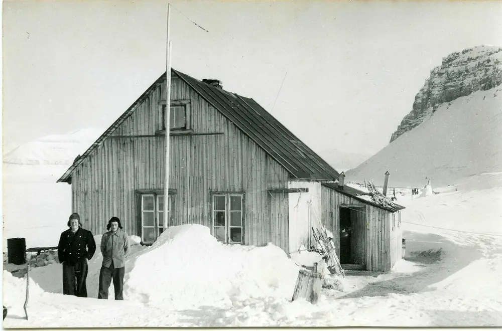 Bildet viser fangstmann Hilmar Nøis sammen med sønnen Johannes Kaps Nøis. De står foran hjemmet/hovedfangststasjon Villa Fredheim. Det er vinter og snø på bildet. Bildet viser at Villa Fredheim var stort og flott til å være en fangststasjon.