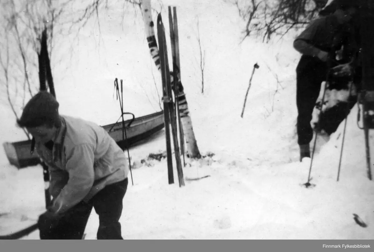 Harald Kjellmo, og Einar Isaksen utenfor gammen i Gokkmokka. Det står oppstilt ski i snøen. En båt, eller kjelke ses i bakgrunnen