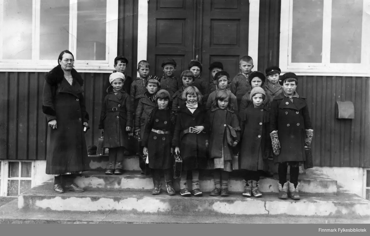 Klassebilde av 2. klasse ved Bjørnevatn skole, oktober 1936. Til venstre står lærerinne Karoline Kristoffersen. I den fremste rekken av barn står fra venstre: Gerd Kjær, Anne Brandzeg, Aud Lund, Elsa Olsen og Margit Nordnes. Fra venstre i den midterste rekken står: Margit Bang Larsen, Petra Halvorsen, Enid Larsen, Astrid Paulsen, Gunvor Jensen og Kåre Sivertsen. I bakerste rekke fra venstre står: Konrad Pettersen, Arnold Hansen, Øyvind Wikland, Birger Olsen Borgelin, Petter Pettersen og Edvin Johansen. Klassen er oppstilt på trappa foran skolen