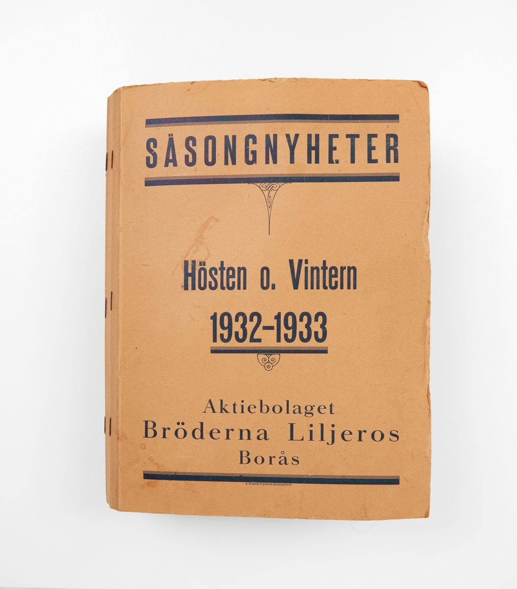 Pärm av papp. Blad med fastlimmade tygprover, uppgifter om material, tygets bredd, namn mm. Text på pärmens framsida:'Säsongsnyheter. Hösten o Vintern 1932 - 1933. Klädningstyger. Aktiebolaget Bröderna Liljeros Borås. AB Borås Tryckeri & Kartongfabrik'.