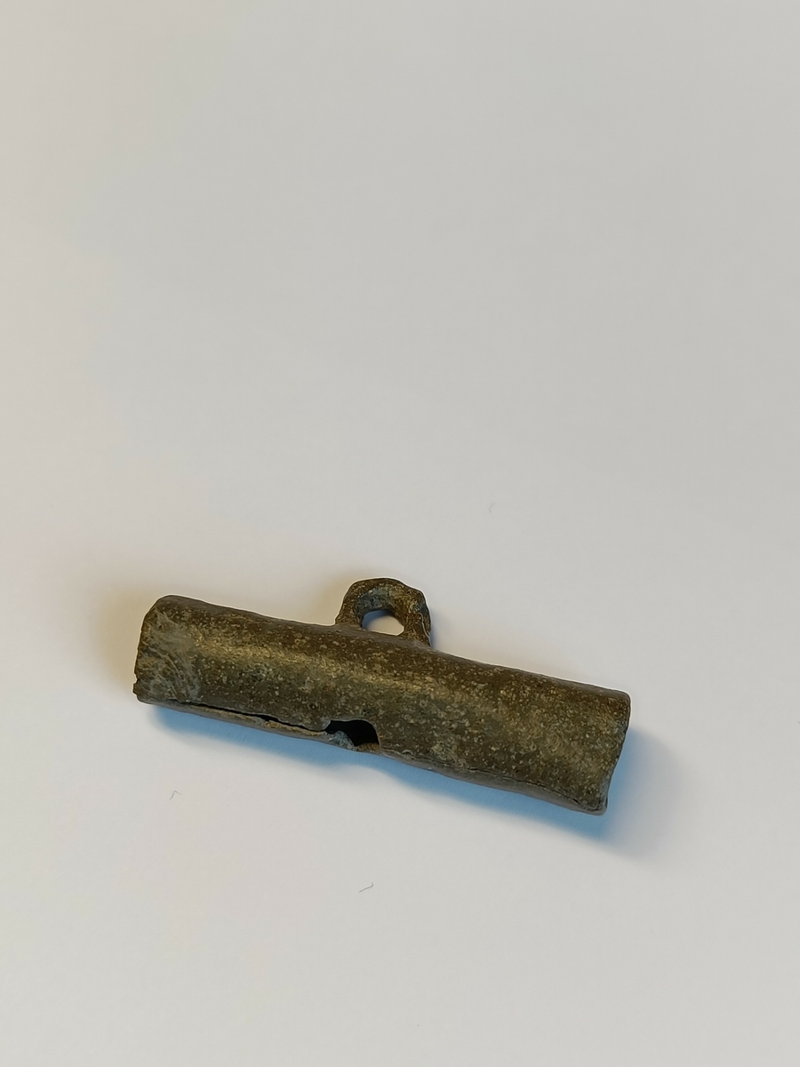 Sylindrisk gjenstand med luftspalte og et øye på oversiden, slik at gjenstanden kan henge i snor. Dette er en lokkefløyte trolig til bruk på fulglejakt; Jerpefløyte.