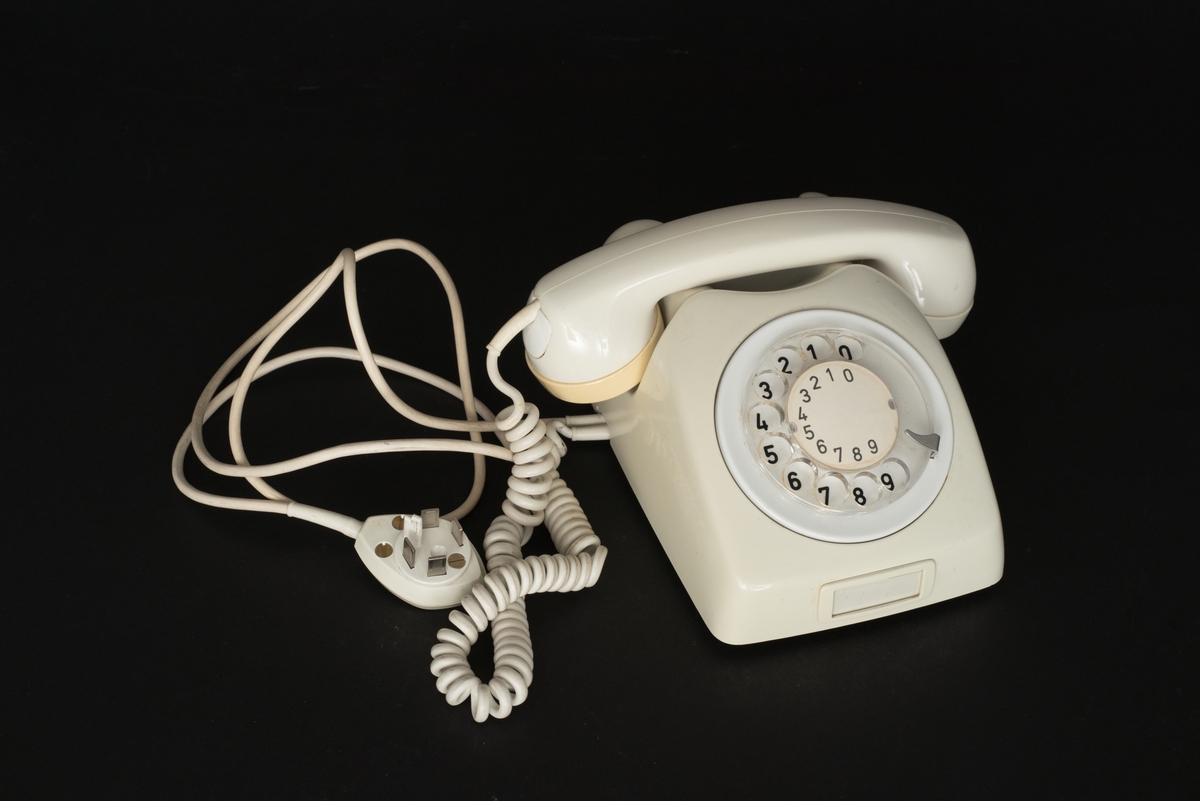 Telefon av gråvit plast med fingerskiva. Lur med spiralformad sladd. Sladd med kontakt. Bottenplatta av metall med inpräglat: Teli MAX MIN och televerksymbol. Siffror under och på nummerskivan.
