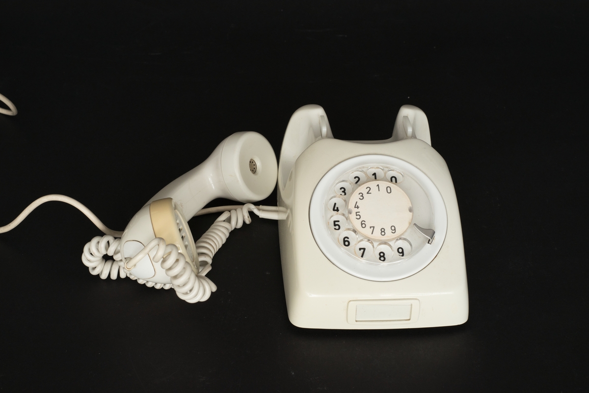 Telefon av gråvit plast med fingerskiva. Lur med spiralformad sladd. Sladd med kontakt. Bottenplatta av metall med inpräglat: Teli MAX MIN och televerksymbol. Siffror under och på nummerskivan.