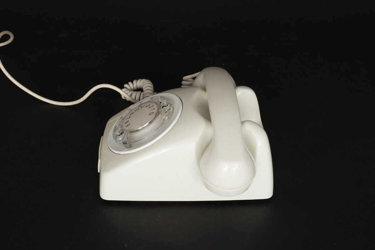 Telefon av gråvit plast med fingerskiva. Lur med spiralformad sladd. Sladd med kontakt. Bottenplatta av metall med inpräglat: Teli MAX MIN och televerksymbol. Siffror under och på nummerskivan.