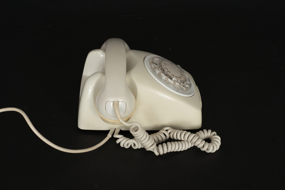 Telefon av gråvit plast med fingerskiva. Lur med spiralformad sladd. Sladd med kontakt. Bottenplatta av metall med inpräglat: Teli MAX MIN och televerksymbol. Siffror under och på nummerskivan.