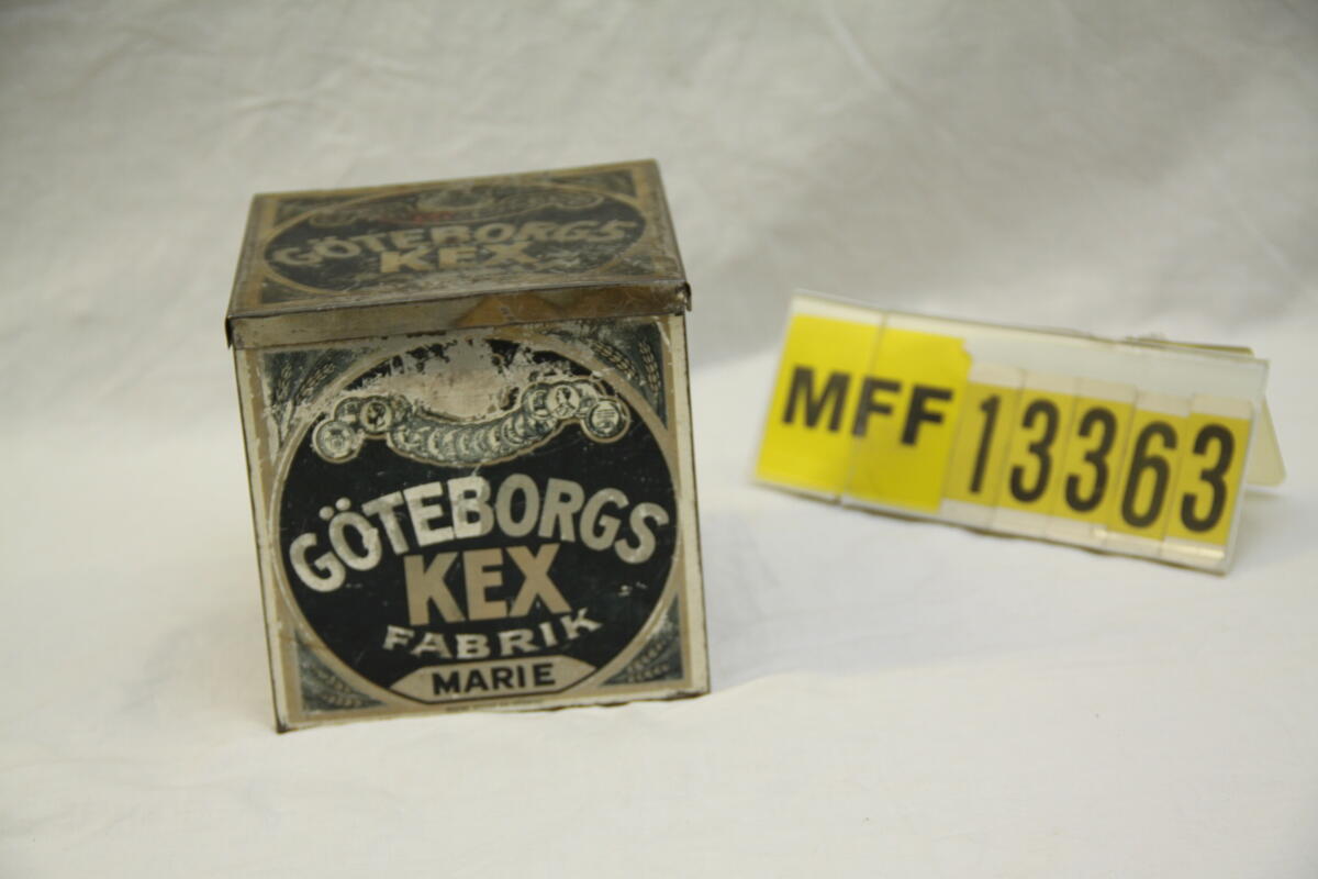 Fyrkantig plåtburk lackerad i svart och silver. Göteborgs kexfabrik Marie på sidorna och på locket. Sigurd Smiths AB Göteborg. Ragnar Forslund på etikett på undersidan.