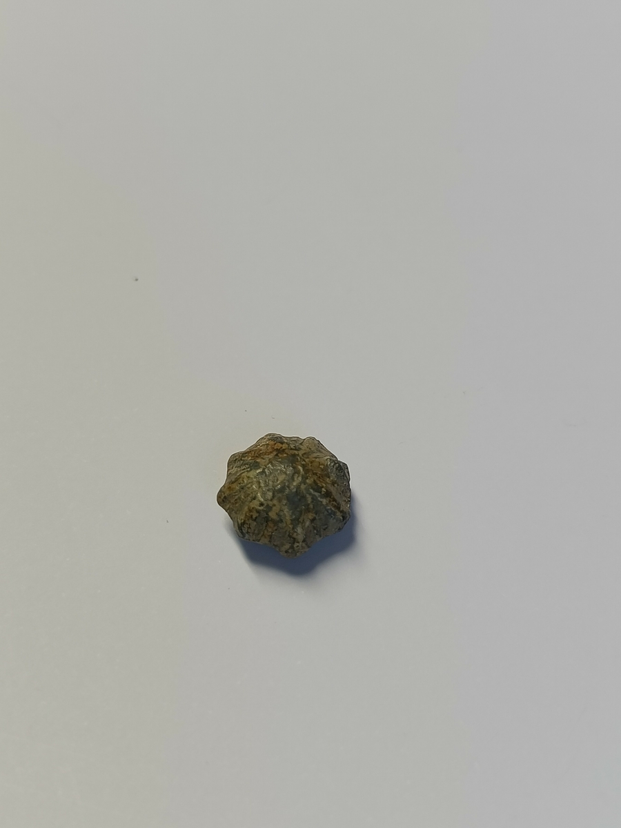 En liten og kuleformet pyntenagle med utforming som en blomst eller stjerne. Selve naglen er borte men hullet til innfestningen er igjen.