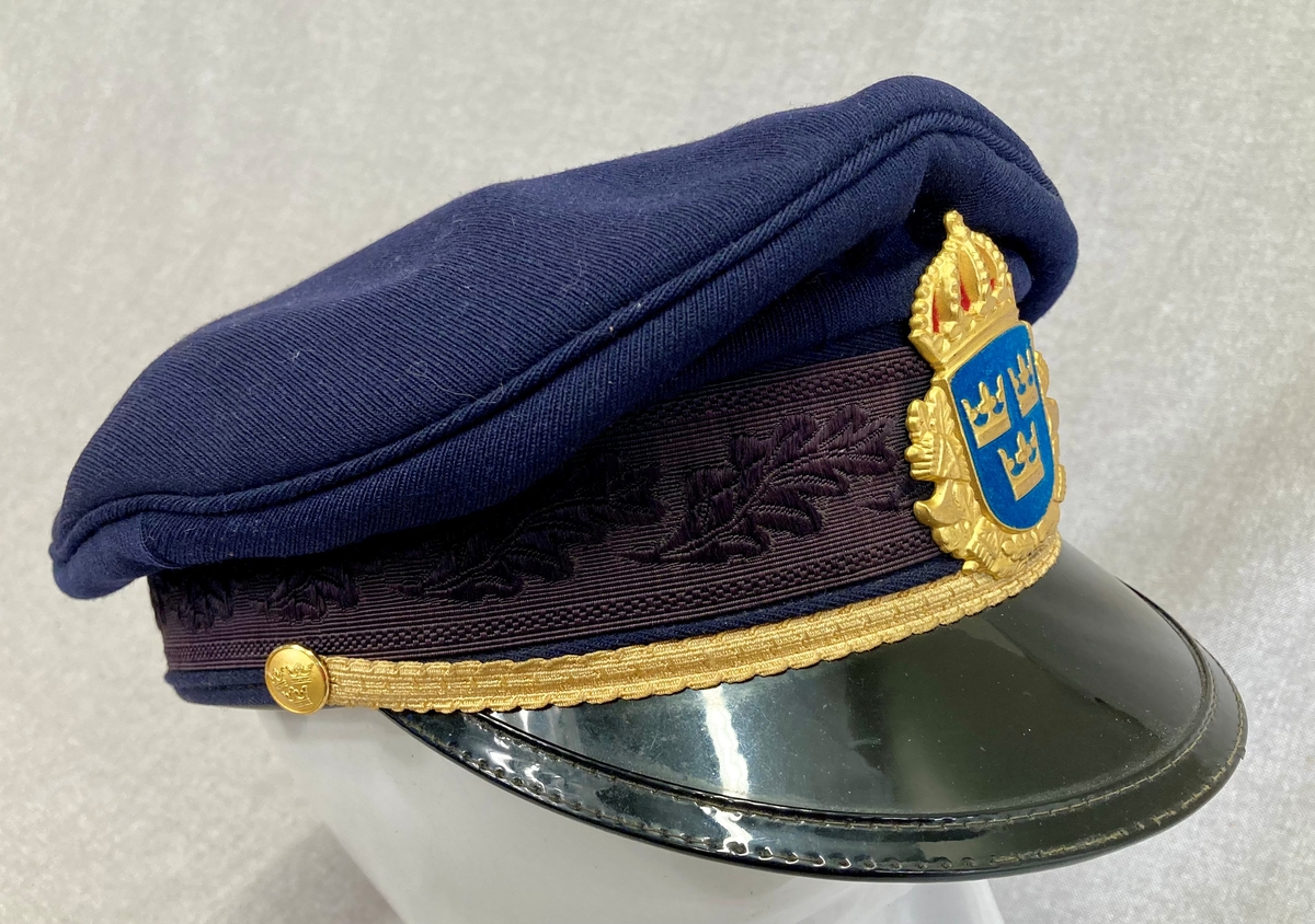 Uniformslue for svensk politi. Mørkeblå med gulldetaljer og svensk politimerking. Luebånd med eikebladsdekor. Blank sort skjerm.