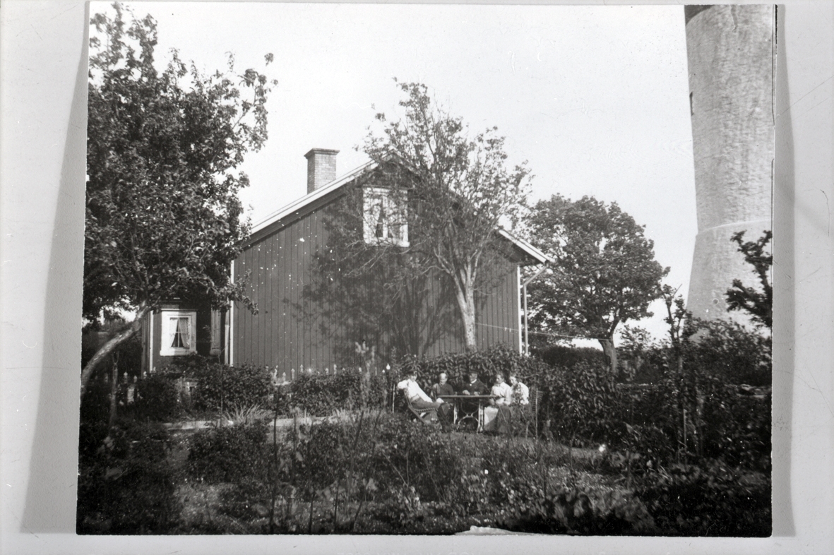 Trädgård vid fyrvaktarhus, Långe Jan. Huset på fotot är fyrmästarbostaden.
Person nr 2 och 3 fr.v, kan vara fyrmästarparet Maria och Peter Olin, som lämnade udden i augusti 1910. Personen längst t.v. kan vara deras son Karl Olin.