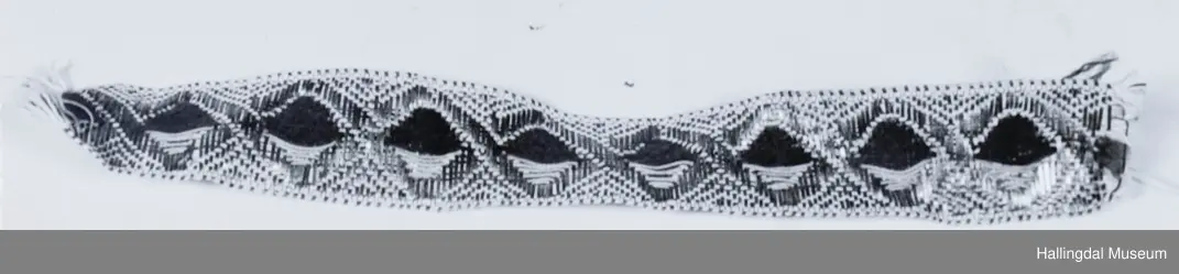 2 siksak border krysser hverandre. I det kvadratiske feltet som oppstår mellom dem er 1 halvpart brodert med rødt ullgarn, den andre med gult lingarn. Lå inni HB 01103.