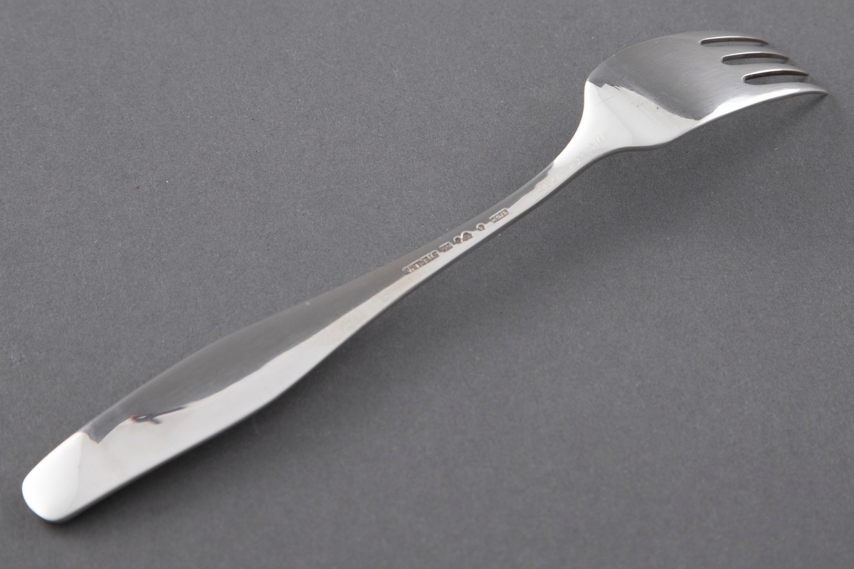 Gaffel i sølv med jevnbredt blad med fire korte tinder fra bladets midte. Flatt skaft som øker ganske sterkt i bredde og minsker lett mot skaftenden. Avrundet og lett oppbøyd skaftende.