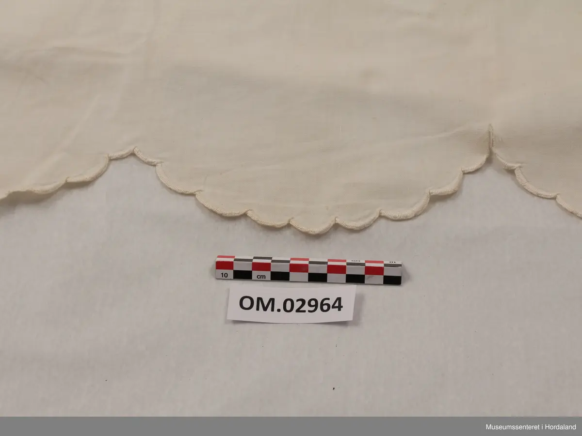 Hvit pyntehåndduk med initialene LM brodert nederst. Øverst er tre ringer formet av sydde hull og brodert blomsterguirlander.