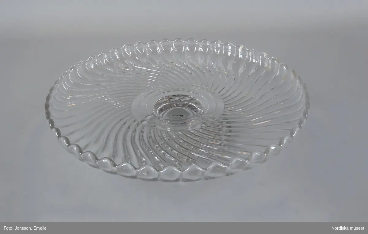 Tårtfat på fot, modell Turbin, från Reijmyre glasbruk. Ofärgat pressglas, pressad yttäckande konvex och konkav dekor av spiralvridna åsar som avslutas i en vågformad kant.  Tillverkade runt sekelskiftet 1900. 
/Cecilia Wallquist  och Kersti Wikström  2010-12-16
