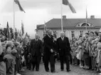 Kung Gustaf VI Adolf på väg upp till Braheparken, flankerad av stadens representanter Thure Ekwall till vänster och Ivar Ekvall till höger. Deras väg är kantad av vuxna och barn med flaggor.