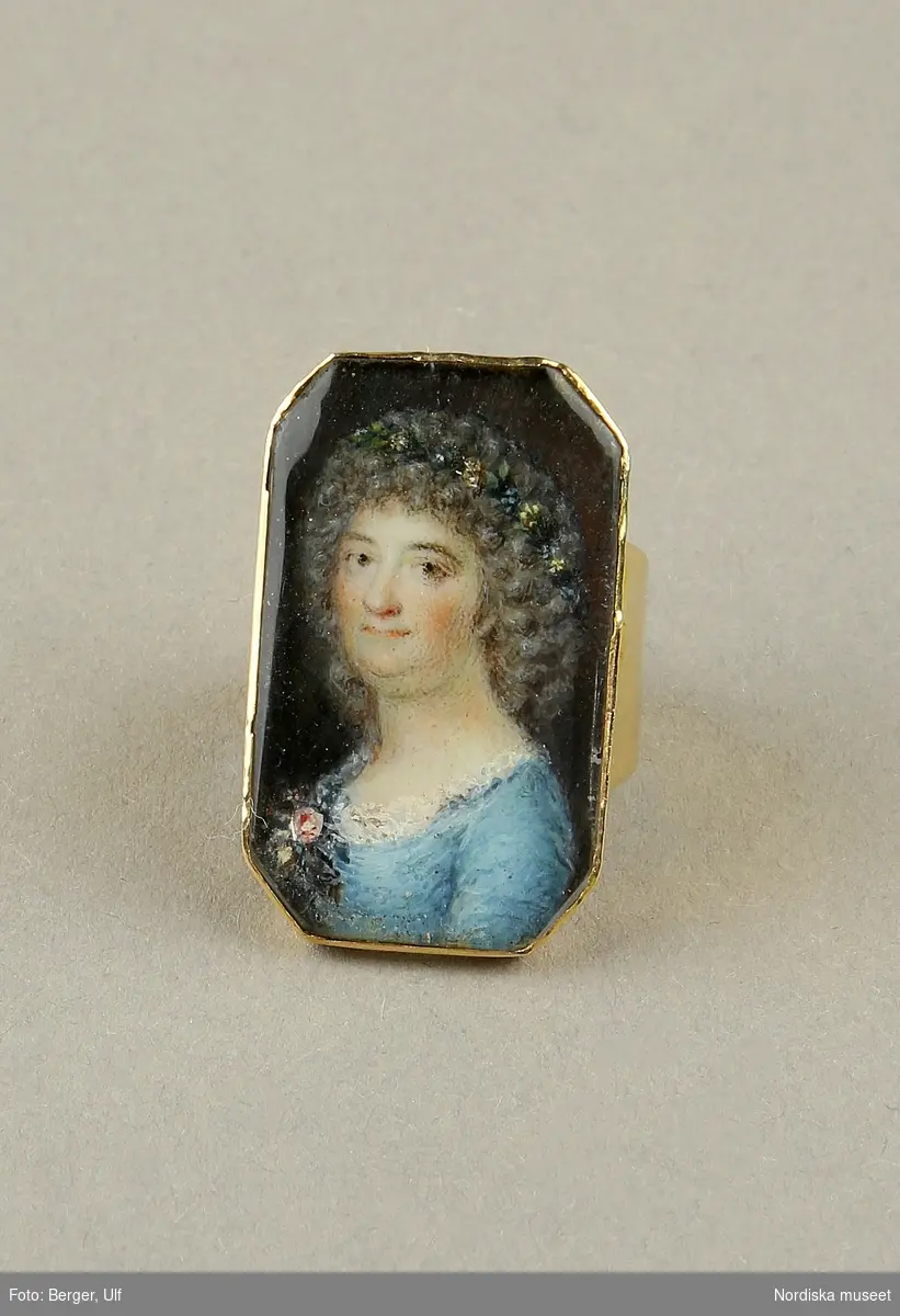  Ring av guld med miniatyrporträtt föreställande Märtha Helena Reenstierna. Målat 1796 på ben i gouacheteknik av Jacob Henric Rönngren (1756-1822) på beställning av M.H.R. även kallad "Årstafrun". Ringen avsedd som gåva till hennnes make ryttmästaren Christian Henric von Schnell på hans namnsdag den 13 november 1796. Graverat C.H.v.S. d. 13 Nov. 1796. 
Monteringen med 18K guld utförd av juveleraren Nils Hofsten. Stämplar: O2 (1796), S:t Erik, NH, 18K,  Kontrollmärke) Sannolikt omarbetad montering 1814.
Porträttet avbildar Märtha Helena Reenstierna i bröstbild sittandes i halvprofil iklädd blå klänning med liten rosenbukett i barmen. Hennes hår är friserat i täta små lockar, håret når nedaför nacken och hon har en smal rosengirlang runt håret. Ögonen bruna. Svagt rosa kinder. Bakgrunden mörk.

Jacob Henric Rönngren var kapten-mecanicus i arméns flotta. Han var född i Finland 1756 men slutade sina dagar i Stockholm 1822. Något dussin av hans miniatyrporträtt är kända - de flesta i Finland och vanligen knutna till officerskåren. Ett porträtt tillhör Finlands Nationalmuseum. I Nationalmuseum, Stockholm, finns sju miniatyrporträtt bl a av gmj Corfitz Beck-Friis (1724-1798), öljt David von Schewen (1770-1841) samt dåv kh i Finska församlingen, Bengt Lange.   

Nils Hofsten blev mästare som juvelerare i Stockholm 1788. Hans ritning till mästerstycke finns på Nationalmuseum. Hofsten stämplade 1795 -1805. Död 1814.
Ingrid Roos 2011-01-17
