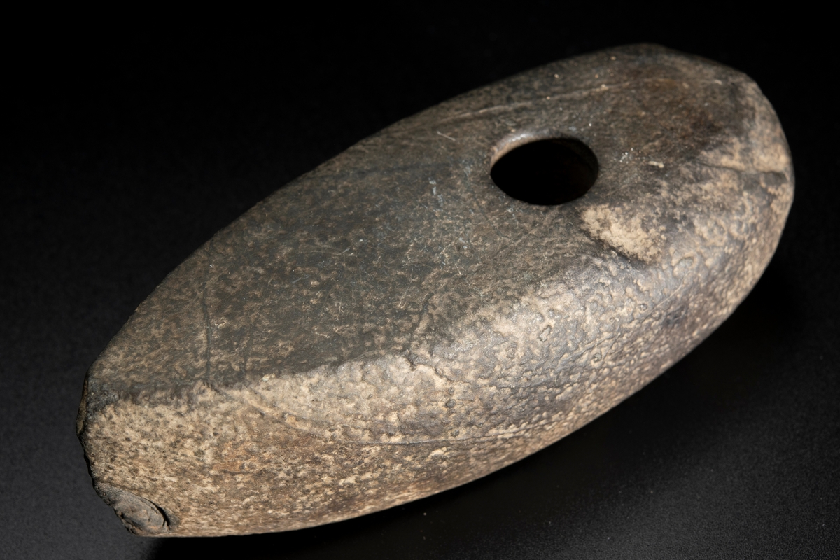 Skafthålsyxa av bergart. Plan ovan- och undersida. Slipad. Yttersta nackpartiet sluttar skarpt.