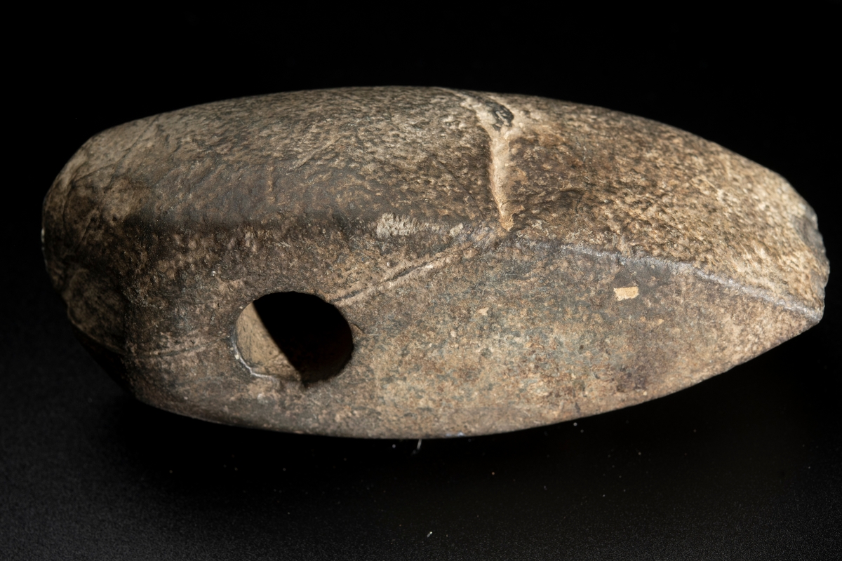 Skafthålsyxa av bergart. Plan ovan- och undersida. Slipad. Yttersta nackpartiet sluttar skarpt.