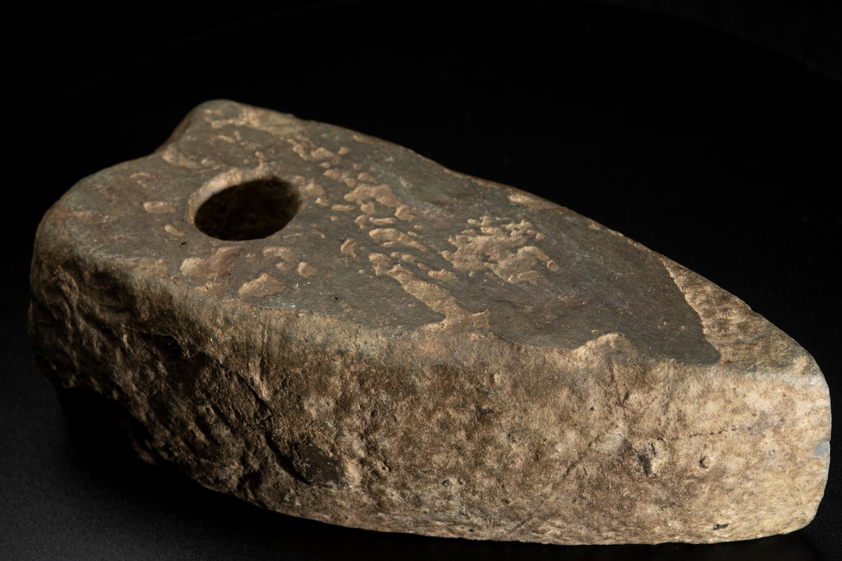 Ett ovanligt stort och klumpigt exemplar. Delvis slipad. Nacken slutar tvärt. Vittrad.