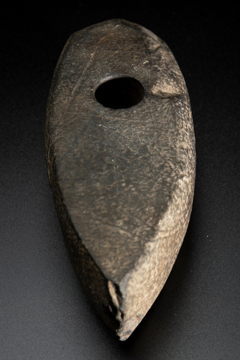 Skafthålsyxa av bergart. Plan ovan- och undersida. Slipad. Yttersta nackpartiet sluttar skarpt.