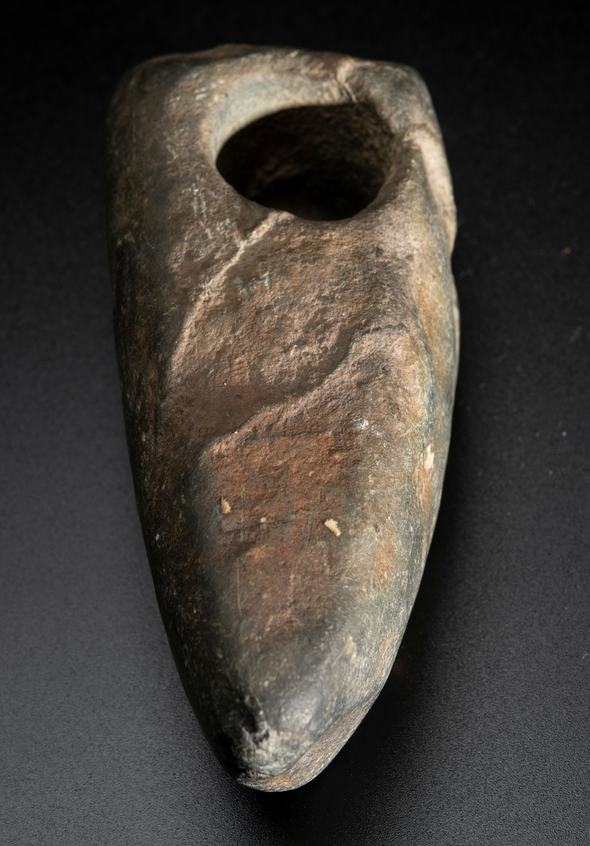 Skafthålsyxa av bergart. Bredast i nacken. Skafthålet placerat långt bakåt. Plan ovan- och undersida.