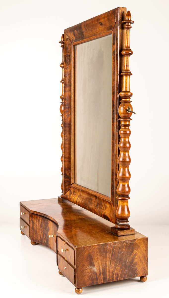 Byråspegel, (lådspegel) av rotmahogny. Med en större och fyra mindre lådor. Svarvade ståndare för spegelns upphängning.