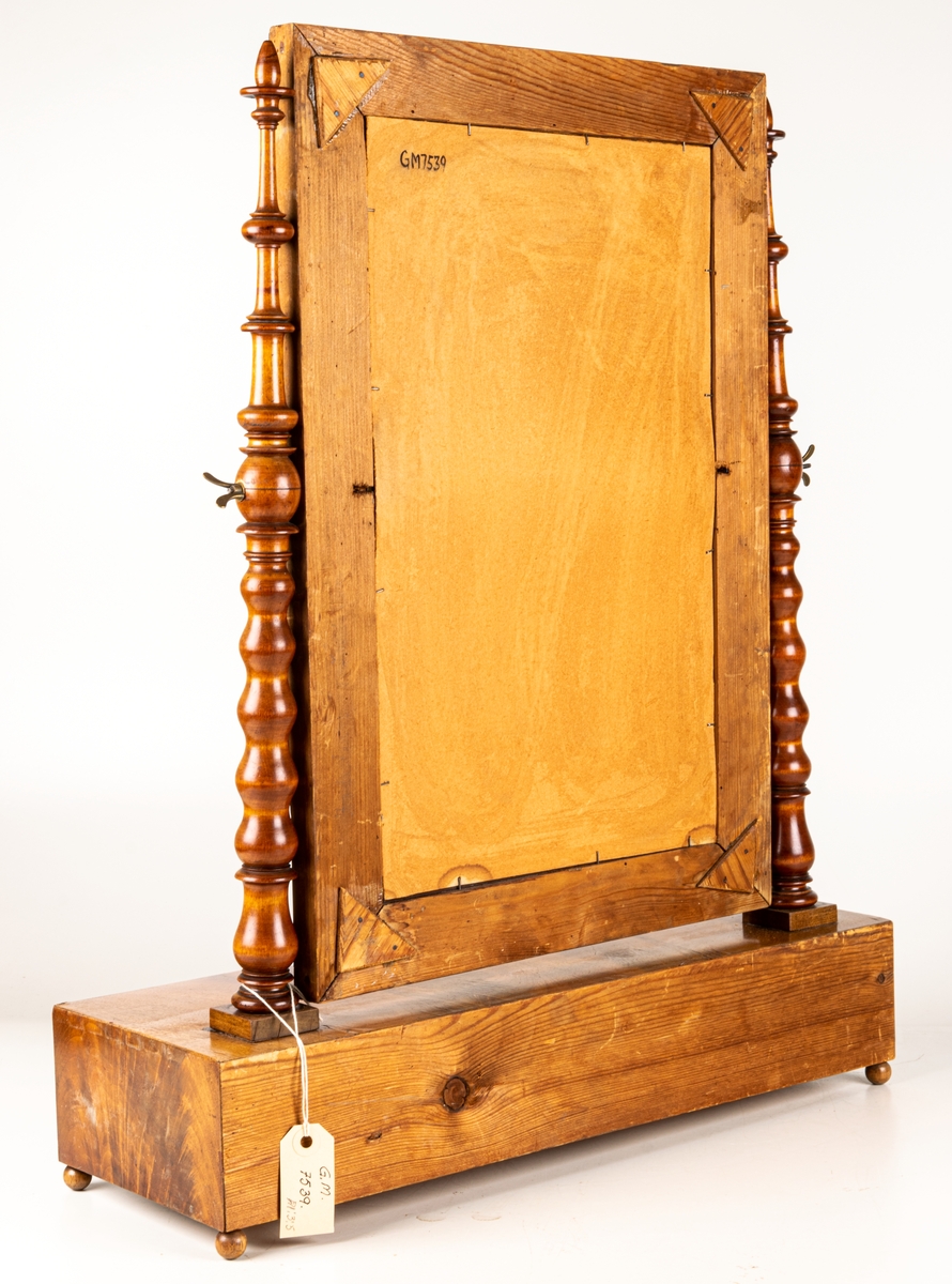 Byråspegel, (lådspegel) av rotmahogny. Med en större och fyra mindre lådor. Svarvade ståndare för spegelns upphängning.