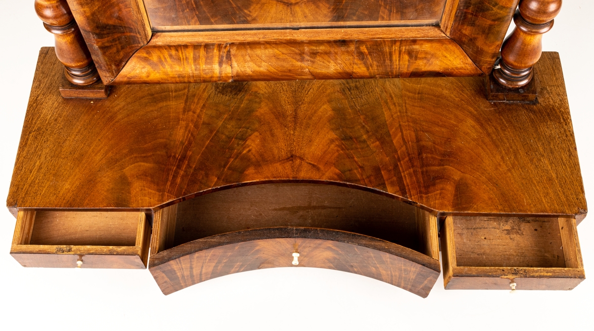 Byråspegel, (lådspegel) av rotmahogny. Med en större och fyra mindre lådor. Svarvade ståndare för spegelns upphängning.