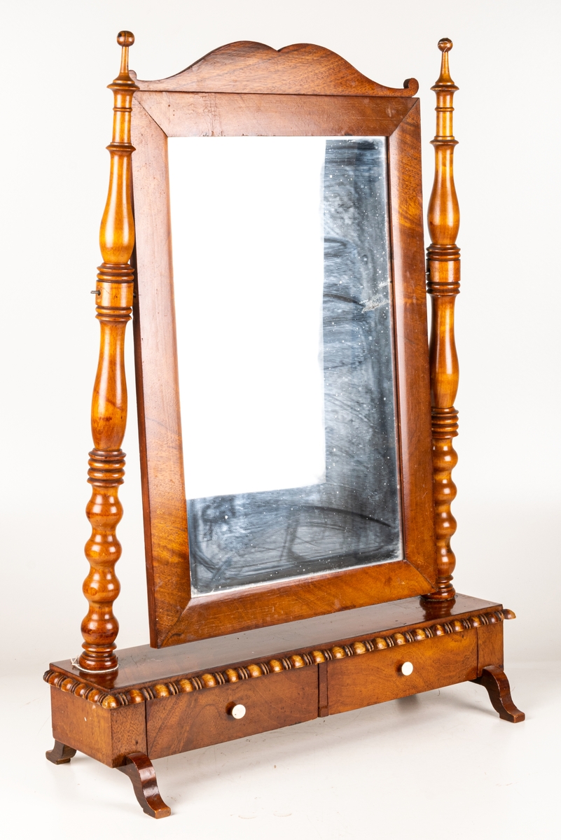 Bordsspegel, brunbetsad. Rektangulär ram med profilerat överstycke. Ramen upphängd på stativ. Två lådor. Svängda fötter. Ostadigt.