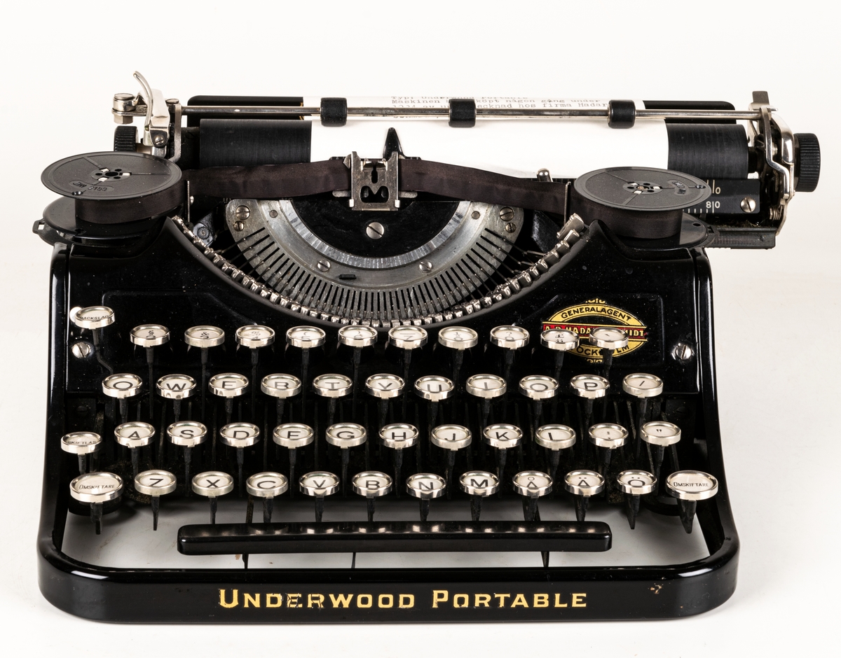 Reseskrivmaskin, Underwood Portable. Svartlackerad plåt. Runda tangenter med text på vit botten under cellulloid och med förnicklade kanter. Text: "UNDERWOOD" resp "UNDERWOOD PORTABLE" i guldfärg samt "A-B HADAR SCHMIDT GENERALAGENT STOCKHOLM". Tillv.nr: 659847.
I svart låsbar låda med bärhandtag. Nyckel saknas.