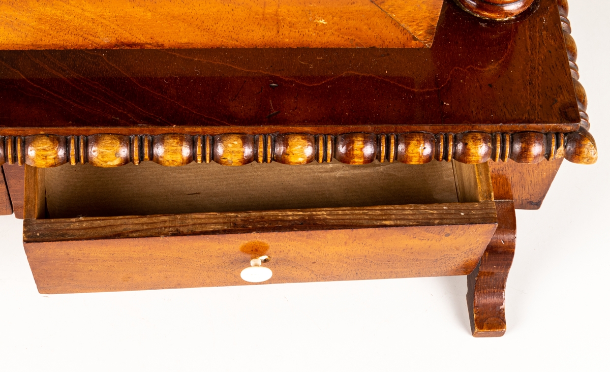 Bordsspegel, brunbetsad. Rektangulär ram med profilerat överstycke. Ramen upphängd på stativ. Två lådor. Svängda fötter. Ostadigt.