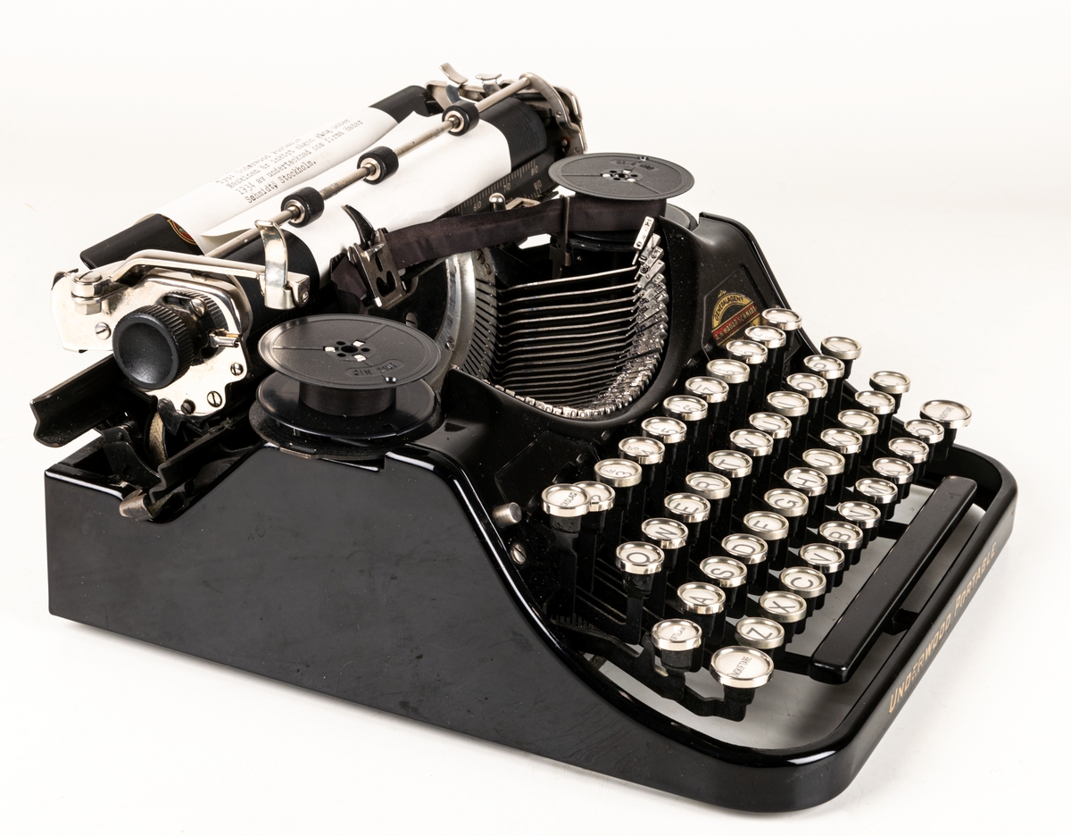 Reseskrivmaskin, Underwood Portable. Svartlackerad plåt. Runda tangenter med text på vit botten under cellulloid och med förnicklade kanter. Text: "UNDERWOOD" resp "UNDERWOOD PORTABLE" i guldfärg samt "A-B HADAR SCHMIDT GENERALAGENT STOCKHOLM". Tillv.nr: 659847.
I svart låsbar låda med bärhandtag. Nyckel saknas.