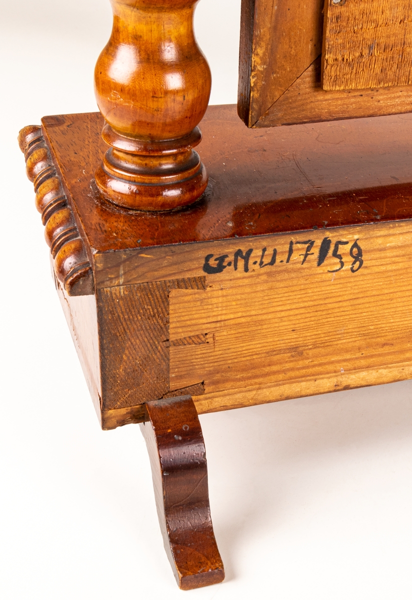 Bordsspegel, brunbetsad. Rektangulär ram med profilerat överstycke. Ramen upphängd på stativ. Två lådor. Svängda fötter. Ostadigt.