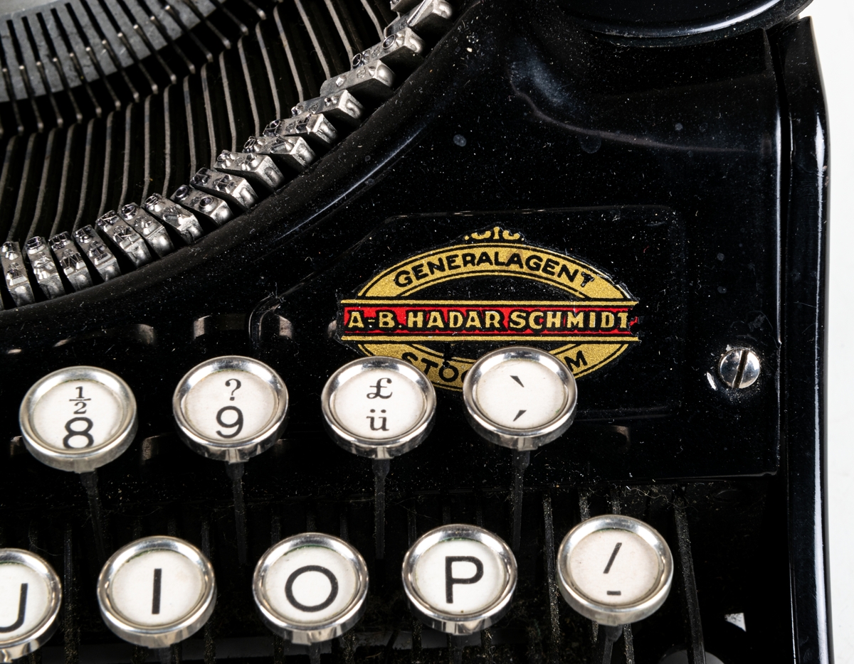 Reseskrivmaskin, Underwood Portable. Svartlackerad plåt. Runda tangenter med text på vit botten under cellulloid och med förnicklade kanter. Text: "UNDERWOOD" resp "UNDERWOOD PORTABLE" i guldfärg samt "A-B HADAR SCHMIDT GENERALAGENT STOCKHOLM". Tillv.nr: 659847.
I svart låsbar låda med bärhandtag. Nyckel saknas.