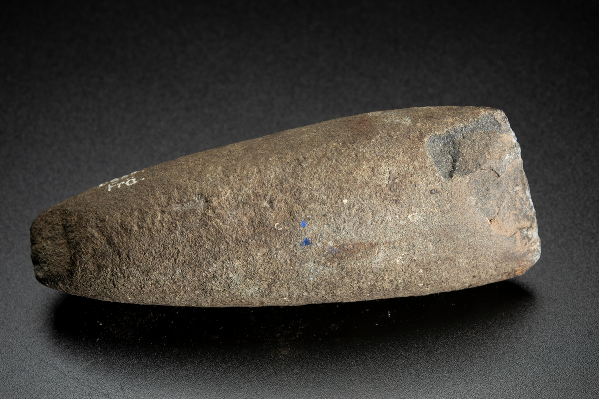 Runt tvärsnitt, den ena eggbildande sidan dock relativt planslipad långt uppåt mot nacken. Avsmalnar mot nacken. Eggen skadad.