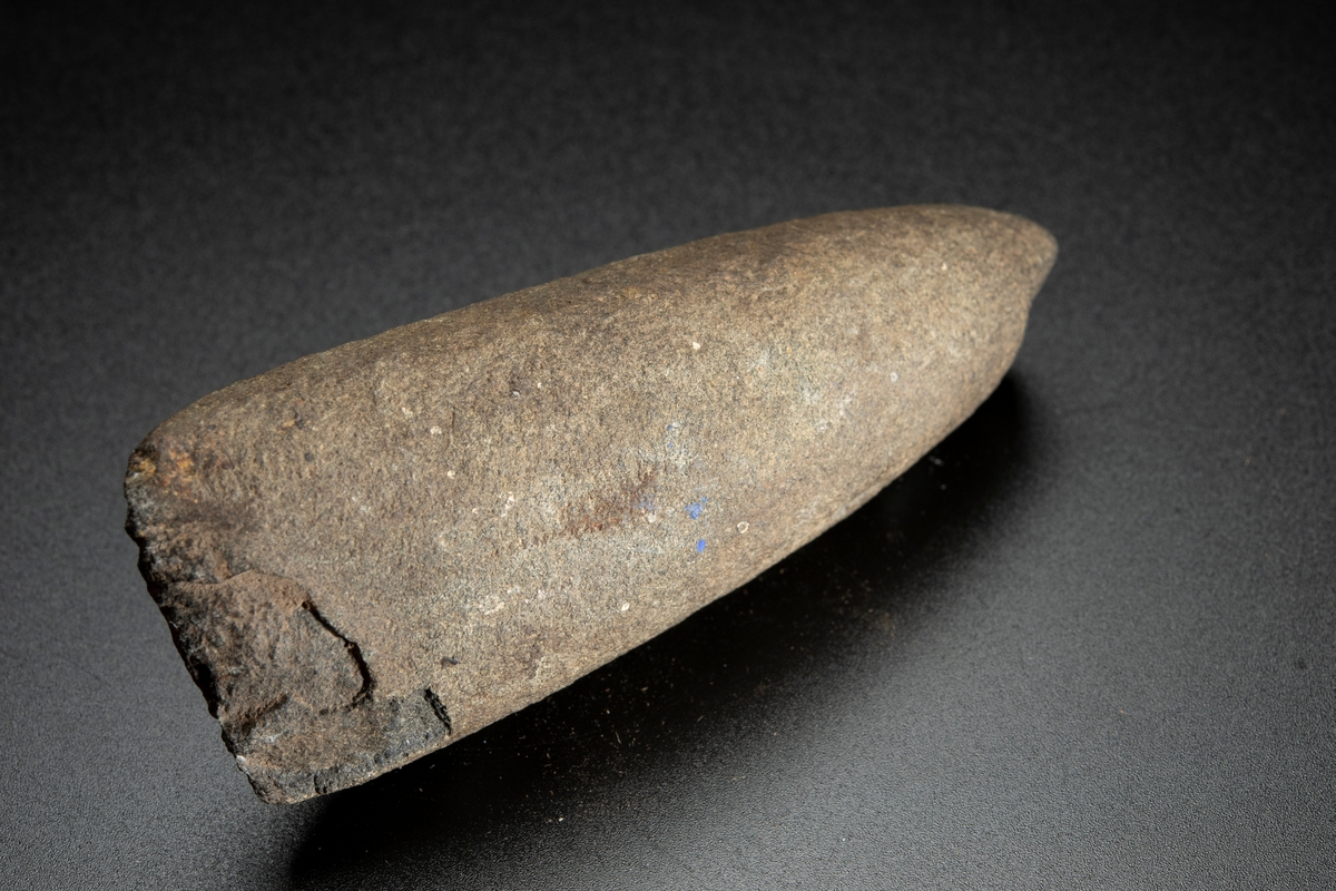 Runt tvärsnitt, den ena eggbildande sidan dock relativt planslipad långt uppåt mot nacken. Avsmalnar mot nacken. Eggen skadad.