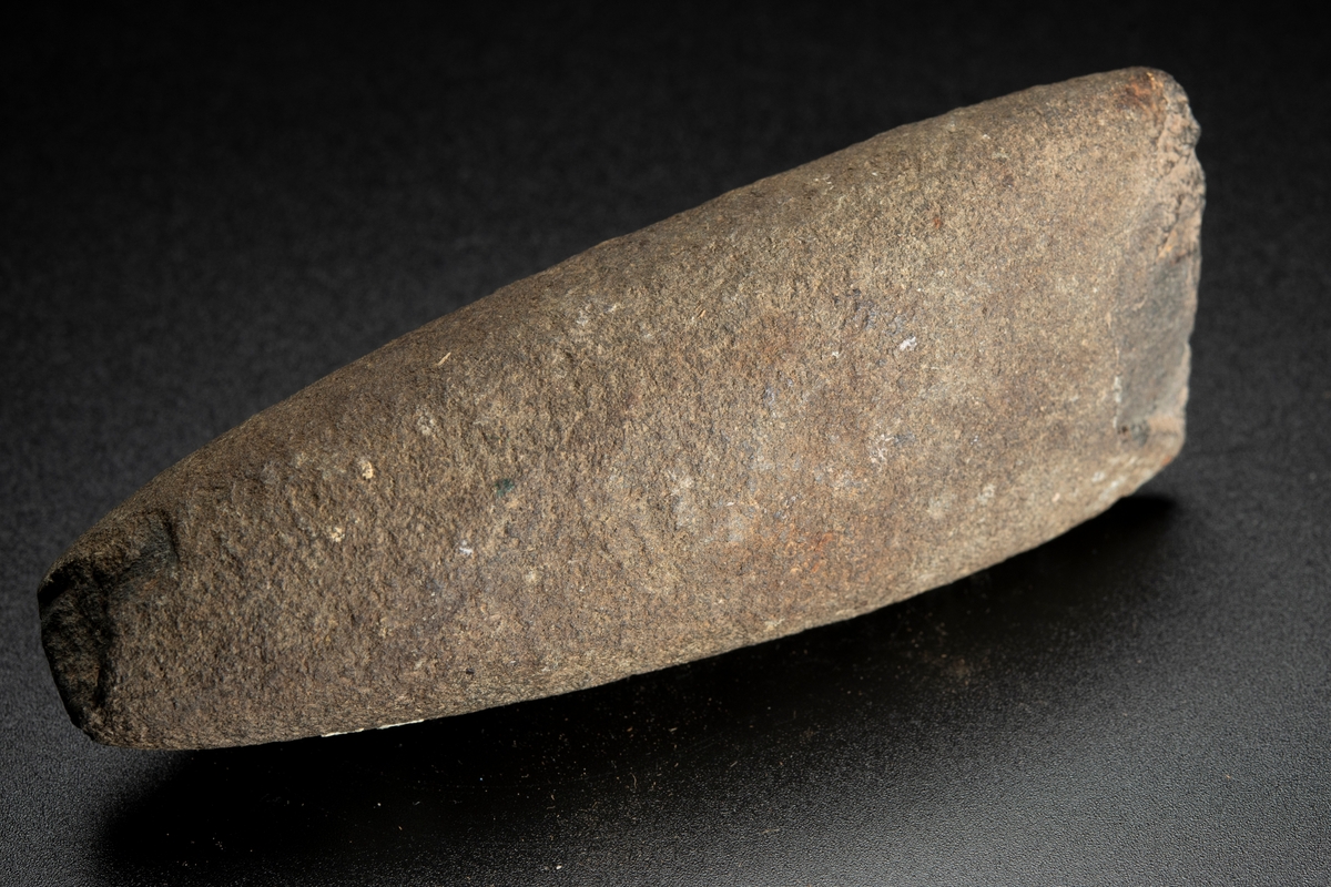 Runt tvärsnitt, den ena eggbildande sidan dock relativt planslipad långt uppåt mot nacken. Avsmalnar mot nacken. Eggen skadad.